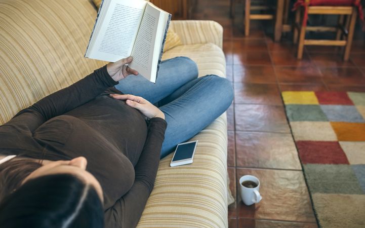 Pregnant woman reading a book lying on the couch