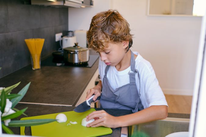 Focused boy cutting fresh onion while cooking in kitchen