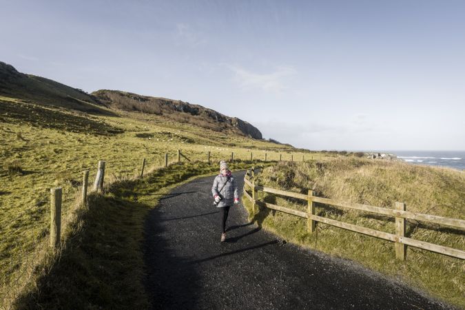 Woman walking on country road between sea and field