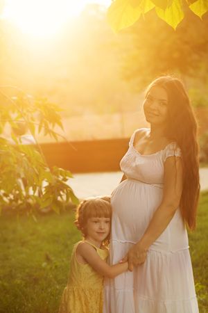 Daughter leaning on her pregnant mother’s stomach