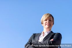 Happy proud businesswoman standing with arms crossed against blue sky 4MXBx5