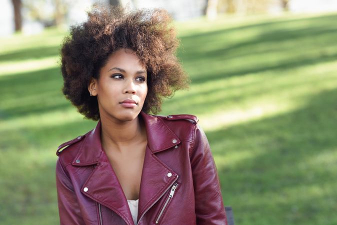 Woman sitting outside in red leather jacket on sunny day with grass in background