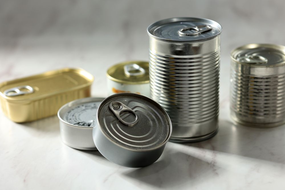 Various Closed Tin Cans with Food Preserves on a Light Gray Background.