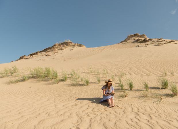 Young woman reading book on sand