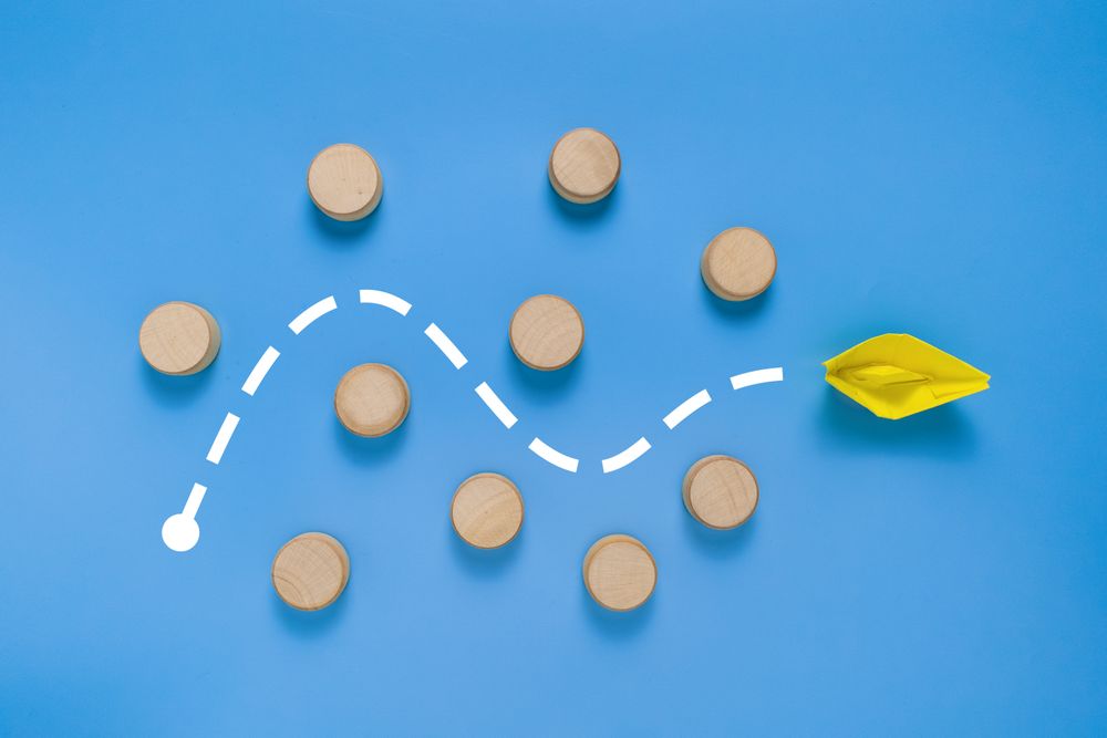 a yellow paper boat passes through barrier. isolated on blue background. concept of avoiding obstacle to achieve a goal