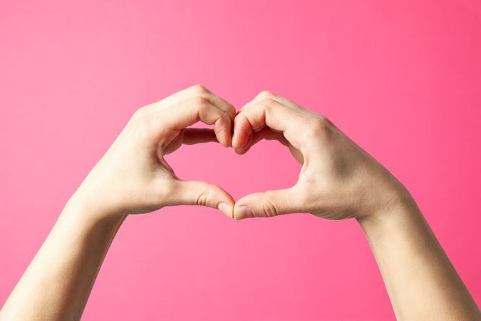 Woman holds hands in the shape of a heart on pink background