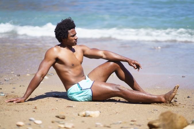 Man in swim trunks relaxing on beach near the water