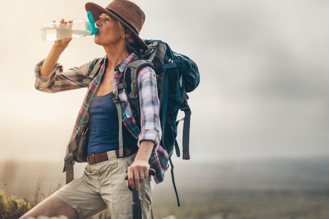 Close up of an older female hiker taking a break during her trek and drinking water