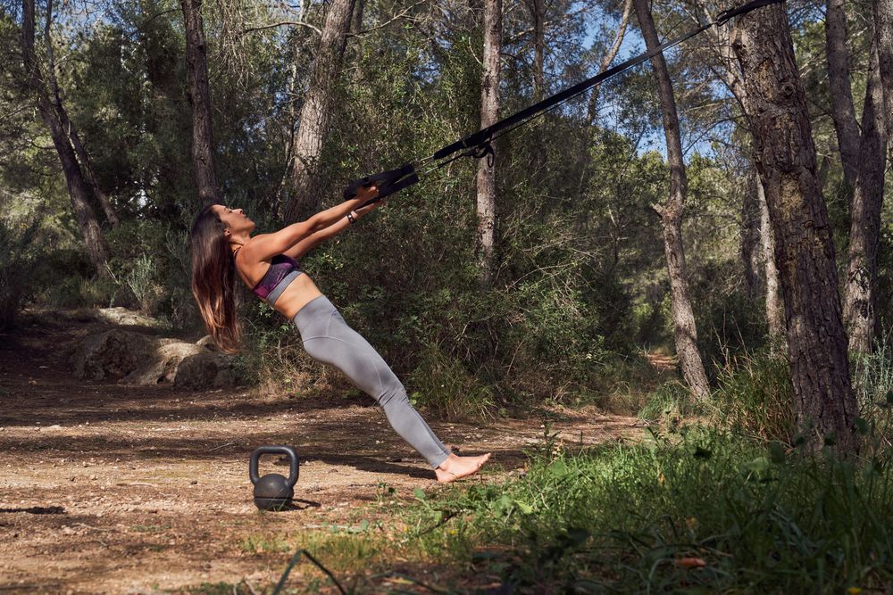 Fit woman exercising in woods using TRX bands