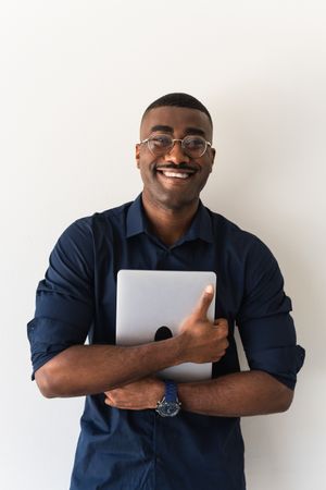 Smiling Black guy with laptop near wall