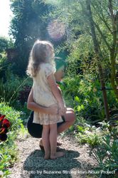 Mother holds daughter around her waist while looking at garden plants 4Azlqb