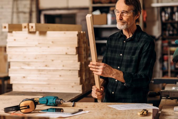 Older man in protective glasses with piece of wood and equipment