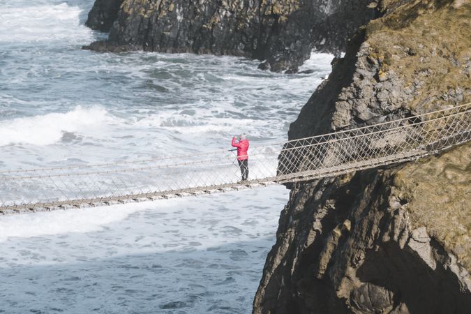 Tourist walking on rope bridge suspended between cliffs in Northern Ireland
