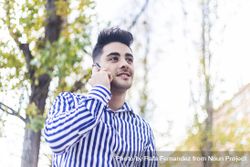 Portrait of young man standing in striped shirt speaking on phone outside 0V6wKD