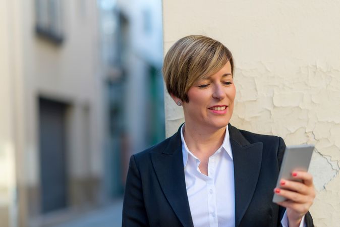 Woman wearing a blazer and checking phone outside