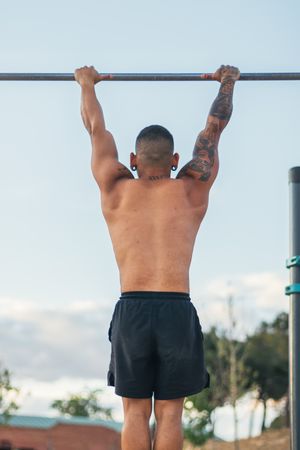 back view of a male athlete doing pull ups on a bar outdoors, calisthenics