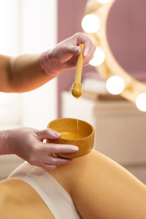 Therapist preparing honey mixture during beauty body treatment.