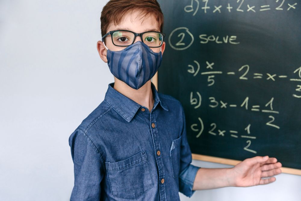 boy with mask in front of a blackboard with equations