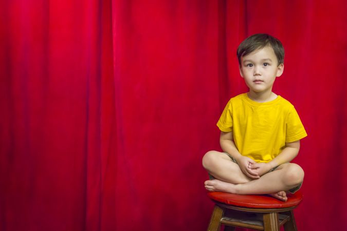 Biracial Boy Sitting on Stool in Front of Curtain