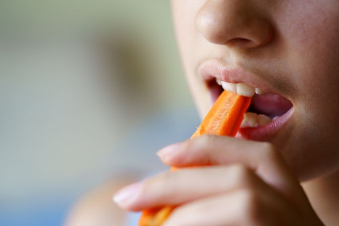 Anonymous teenage girl biting carrot stick