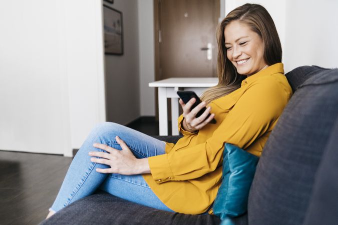 Beautiful adult female sitting on sofa while checking smartphone