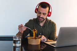 Positive man in headphones eating noodles
