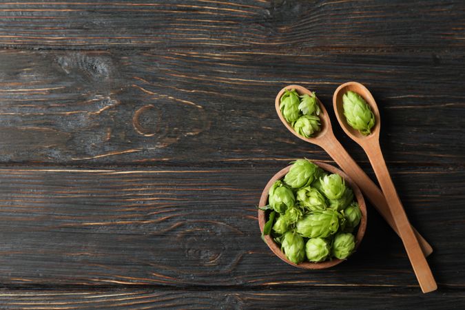 Wooden bowl and spoons with hop on wood background, copy space