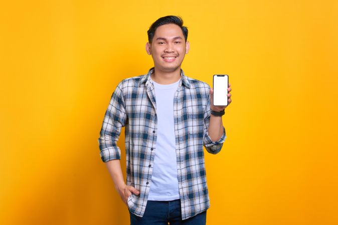 Happy Asian male with hand in pocket and showing blank screen of smart phone