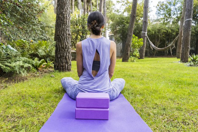 Back view of a woman in sportswear sitting on her yoga mat.