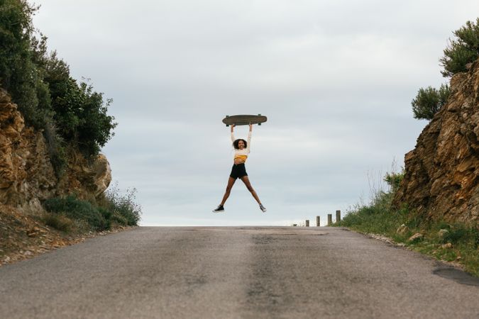 Joyful woman jumping high with longboard