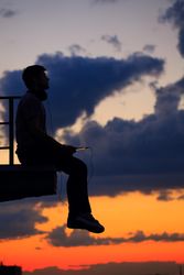 Out line of male sitting on ledge against a colorful dusk side, vertical