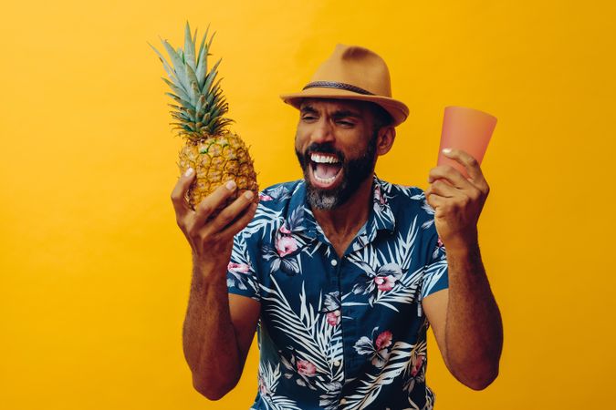 Excited male holding up a pineapple and orange cup