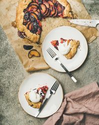 Two plates of fruit tart with whipped cream, forks, knife, on parchment paper