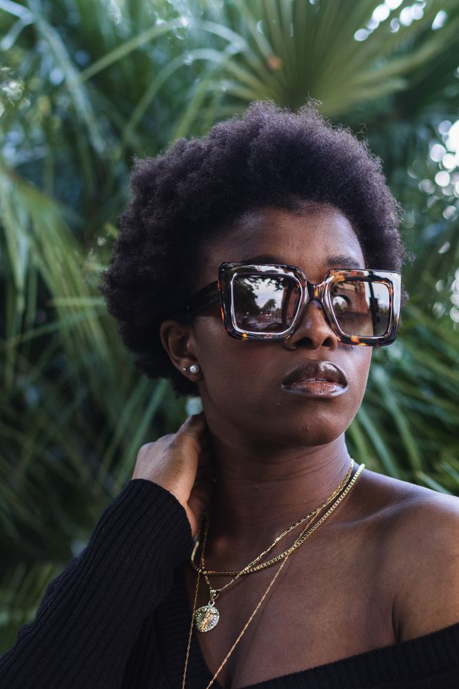 Confident Black woman in sunglasses against greenery