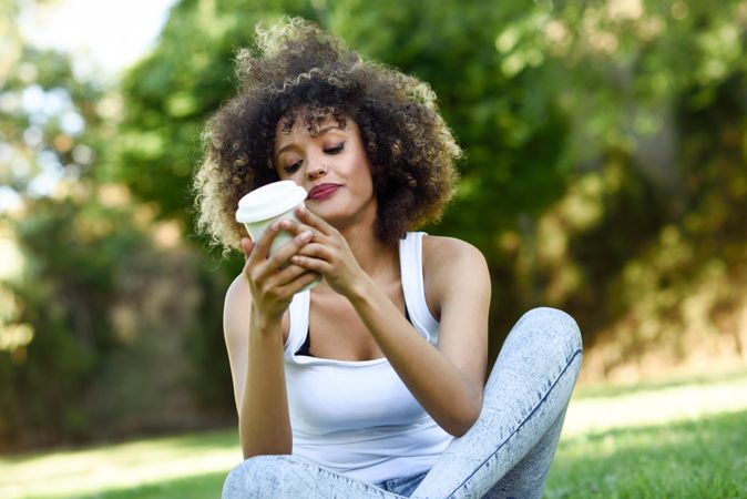 Black woman with afro hairstyle relaxing in park looking at her coffee