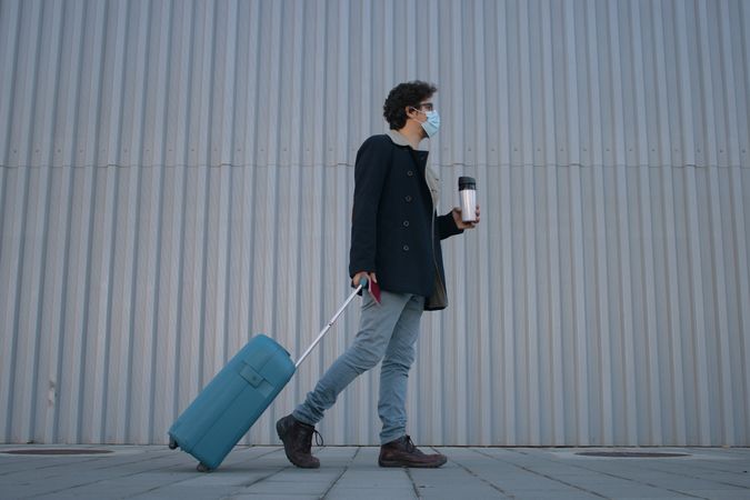 Man with facemask dragging a suitcase