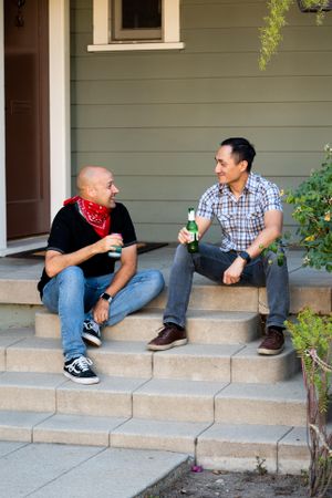 Two men talking and enjoying a beer sitting on porch steps