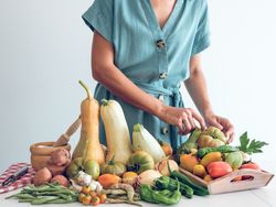 Crop woman putting raw vegetables on kitchen table
