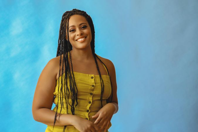 Smiling female with long braided hair and hand to her torso in yellow clothes