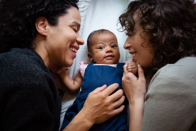 Close up of two smiling moms lying with cute infant