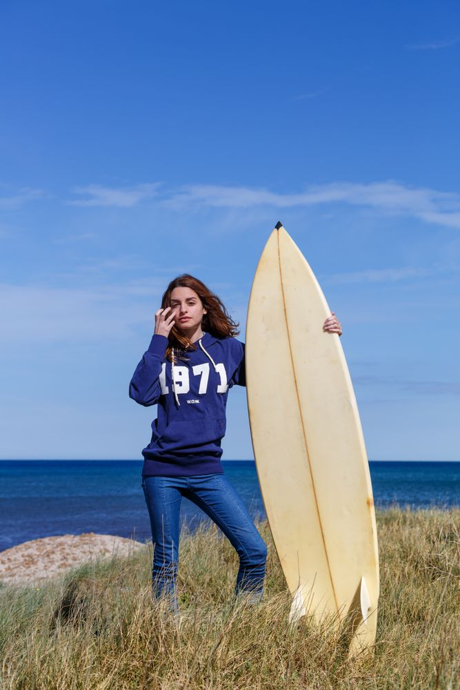Woman with surfboard in seaside with dry vegetation