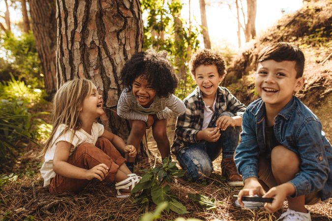 Group of cute kids sitting together in forest and looking at camera