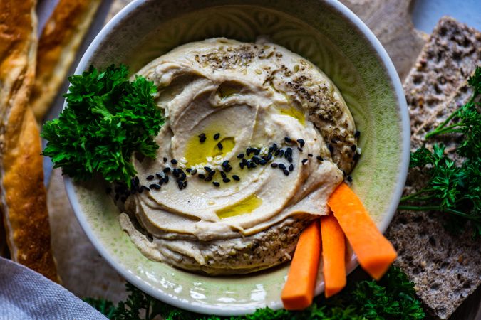 Top view of hummus dip in bowl on board served with veggies and crackers