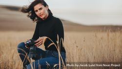 Woman photographer with camera crouching in a dry grass field 4jrDv4