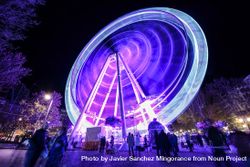 Purple lit ferris wheel with people walking around park bDy9Q0