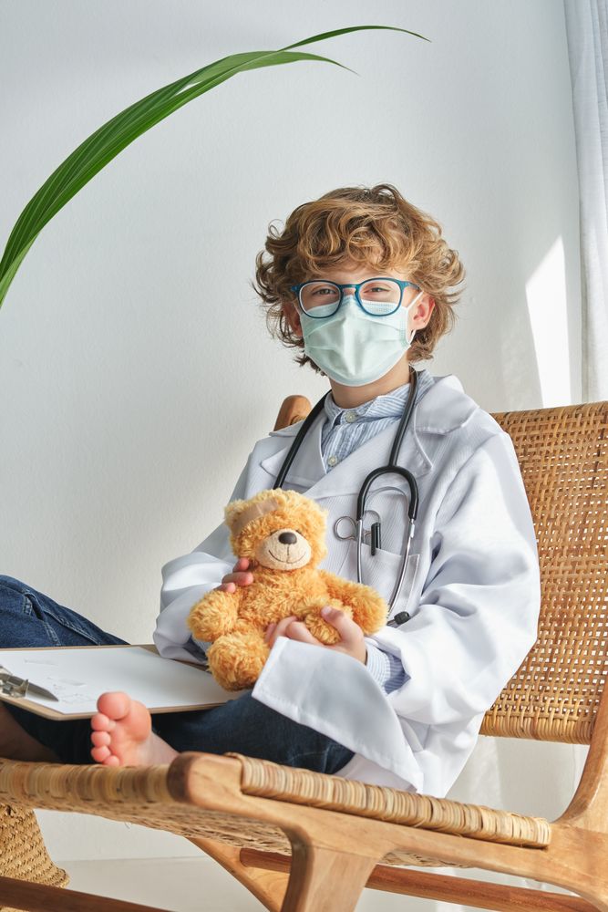 Boy doctor with toy bear on chair on white background