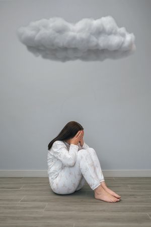 Woman with mental health problems covering her face with hands under a dark cloud