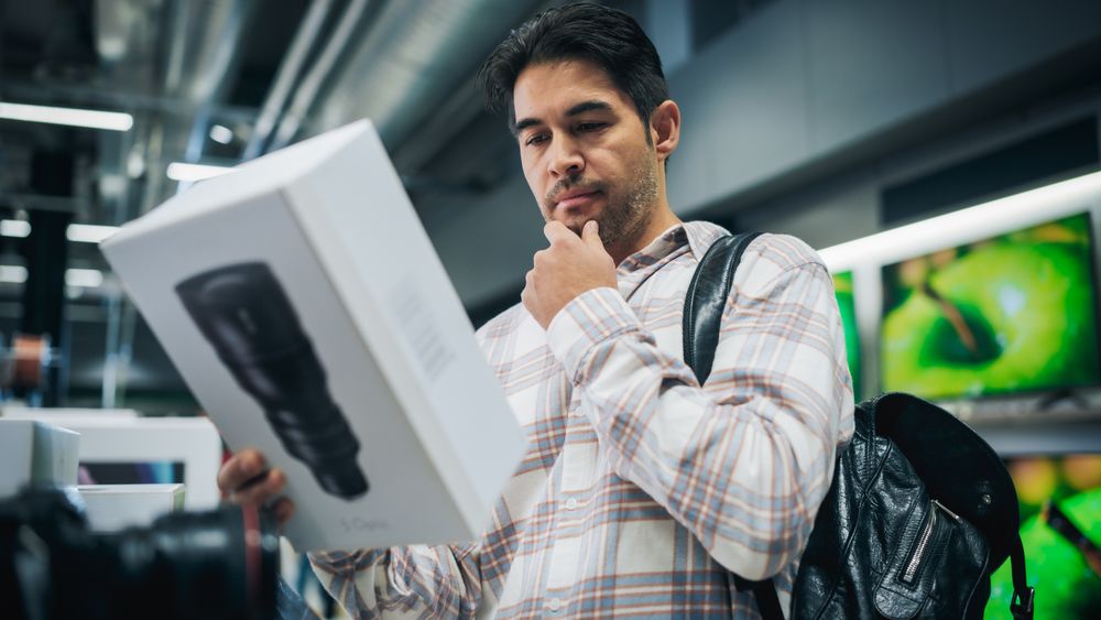 Young Man Shopping for a Camera Lens in Home Electronics Store.