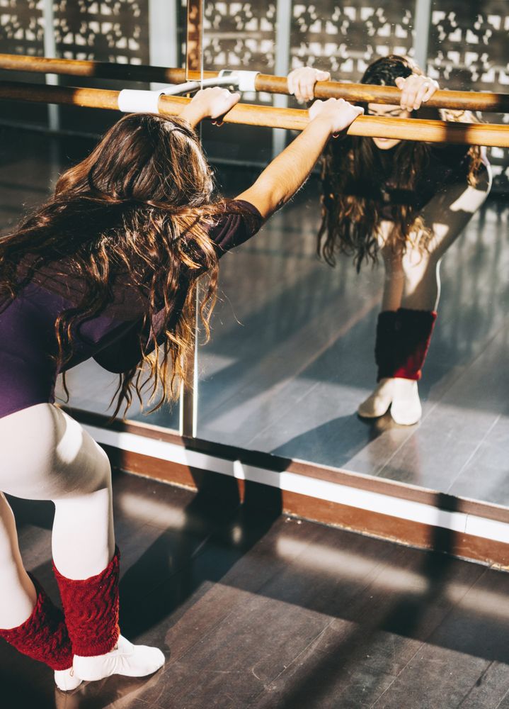 Ballerina dancer warming up flexible body in sunny studio.