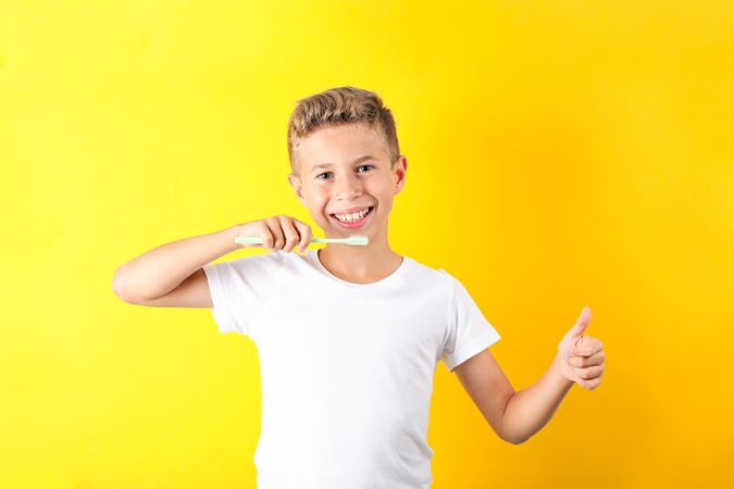 Boy with toothbrush on color background, space for text